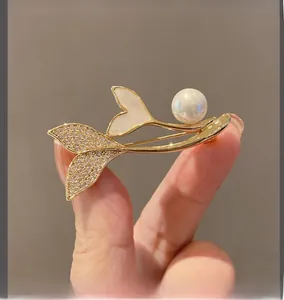 Detail of fishtail brooch featuring gold metal, white mother of pearl and a large round pearl