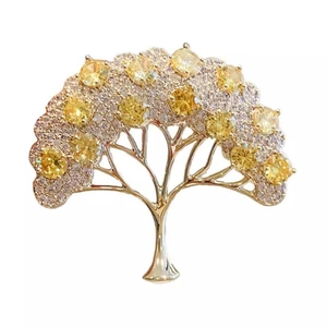 Spilla a forma di albero dorato con pietre gialle e cristalli bianchi su sfondo bianco