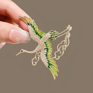 Macro detail of crane brooch with green enamel wings and sparkling zircon inlay