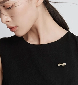 Exquise broche nœud dorée avec strass portée sur une robe noire sans manches