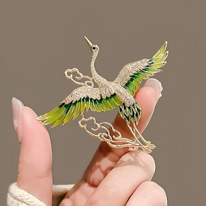 Close-up of crane brooch featuring green enamel wings and sparkling crystal inlay