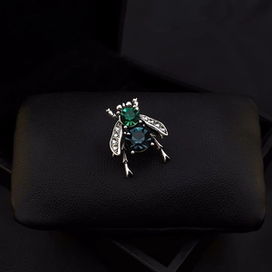 Detailed close-up of a vintage bee brooch with green and blue crystals on black leather