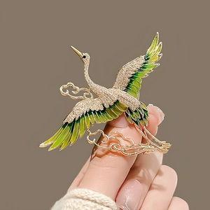 Detail of elegant gold crane brooch with green enamel wings and white rhinestones