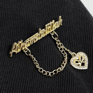 Macro detail of golden Alhamdulillah brooch with chain and rhinestone heart on black fabric