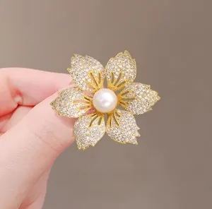 Makro-Detail einer goldenen Blumenbrosche mit Zirkonia-Besatz und großer weißer Perlenmitte