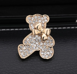 Détail d'une broche ours en peluche dorée ornée de strass sur fond en cuir noir