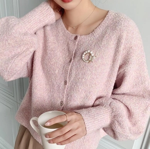 Detail einer Perlenring-Brosche mit Schmetterling auf einer rosa Strickjacke Damen
