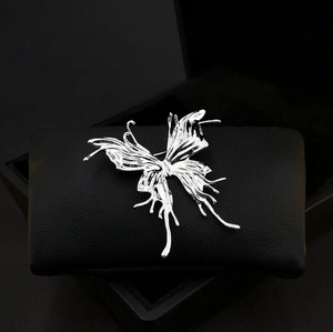 Detailed close-up of a silver butterfly brooch with a liquid metal texture on leather