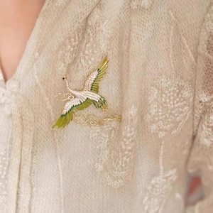 Elegant crane brooch with white crystals and green enamel on beige lace outfit