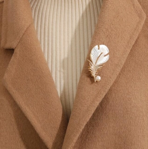 Détail de broche plume avec zircon et perle épinglée sur le revers d'un manteau beige