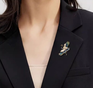 Dettaglio della spilla a forma di gru dorata con smalto blu su un elegante blazer nero