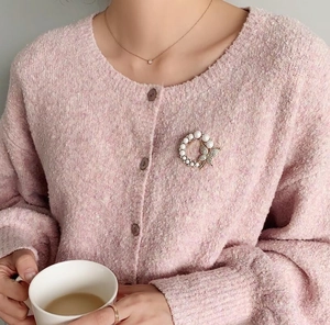Detailansicht der Perlen-Schmetterlings-Brosche an einer rosa Strickjacke im Alltag