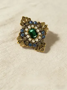 Dettaglio macro di una spilla vintage con cristallo smeraldo, perle e fiori incisi