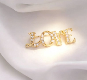 Macro detail of gold LOVE brooch featuring sparkling rhinestones on elegant silk fabric