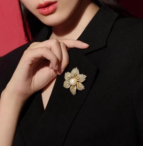Detailansicht einer goldenen Blumenbrosche mit Kristallen und Perle am schwarzen Sakko