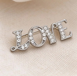 Elegant silver LOVE brooch with sparkling crystal pavé stones on white textured fabric
