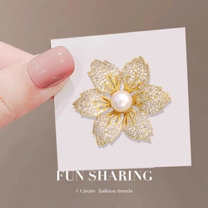 Eleganter goldener Blumenanstecker mit Zirkonia und Perle auf weißer Karte präsentiert