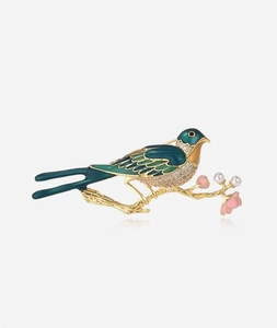 Detail of green enamel bird brooch with white pearls and pink flowers on golden branch