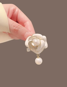Vue détaillée d'une broche camélia en émail blanc avec croissant doré et perle pendante