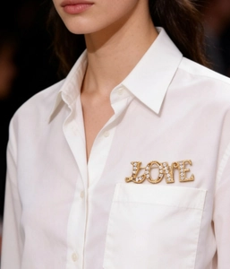 Detailed close-up of a gold LOVE brooch with white zircons on a white shirt pocket