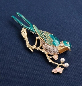 Macro detail of enamel magpie bird brooch with green feathers and white pearls on gold branch