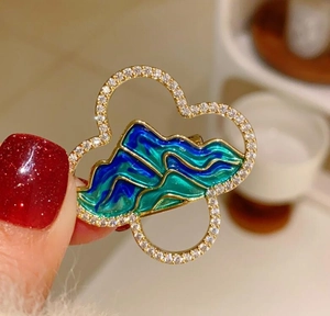 Macro view of Chinese landscape brooch with shimmering zircon and blue enamel details