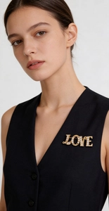 Close-up of a gold LOVE brooch with white crystals on a black suit vest for women