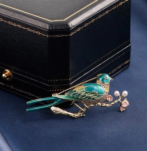 Detailed macro of a green enamel magpie brooch with rhinestones and pearls on a branch
