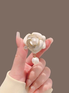 Détail de la broche camélia avec pétales en émail blanc et pendentif perle suspendu