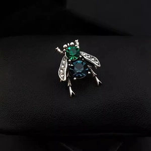Vintage crystal bee brooch with emerald and navy stones on a dark leather background