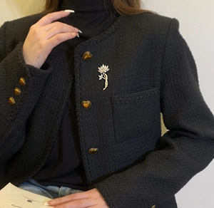 Détail d'une broche lotus aux pétales argentés sur un blazer noir en tweed chic