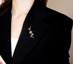 Close-up of a panda and bamboo brooch with green leaves on a black suit lapel