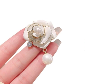 Détail de la broche camélia avec pétales dorés et élégant pendentif en perle suspendue