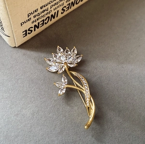 Détail macro de l'élégante broche lotus dorée avec cristaux marquise sur fond texturé