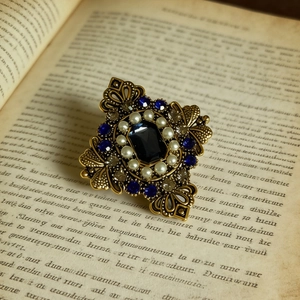 Vista macro della spilla vintage reale con cristallo blu e perle su un libro d'epoca