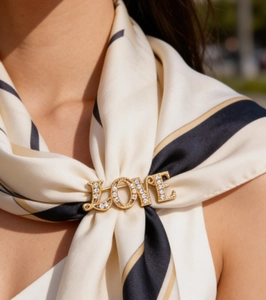 Close-up of golden LOVE brooch with crystals pinned on a striped silk scarf