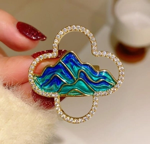 Detail showing hand-held mountain landscape brooch with blue enamel and sparkling crystals
