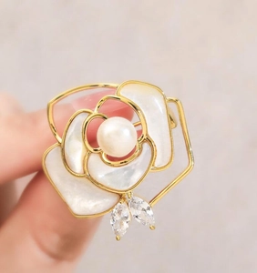 Macro shot of camellia flower brooch with gold frame, white petals and central pearl