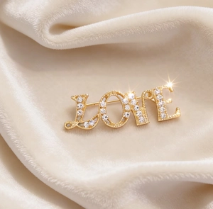 Macro shot of gold LOVE brooch with white rhinestones on beige velvet fabric