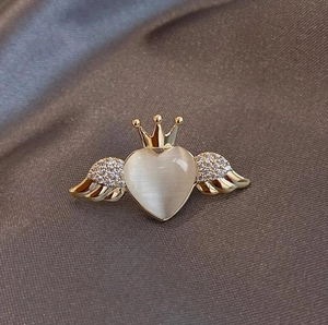 Close-up of golden angel wing brooch with heart cat-eye stone and crown detail