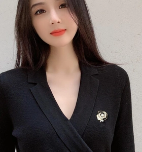 Close-up of a white camellia brooch with gold metal edges worn on a black V-neck sweater