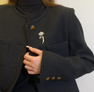 Détail d'une broche fleur dorée sertie de zircons sur un revers de manteau en tweed