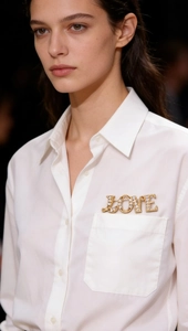 Detail of a golden LOVE letter brooch with sparkling white rhinestones on a white shirt