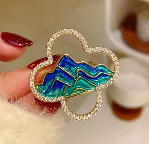 Detail of a landscape brooch with gold clouds, blue enamel waves, and micro-set diamonds