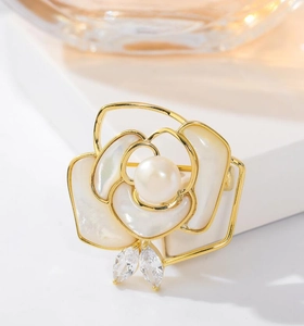 Macro view of gold rose brooch featuring iridescent mother of pearl and pearl detail