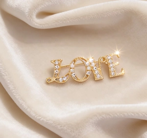 Macro detail of gold LOVE brooch with white rhinestones on beige velvet background