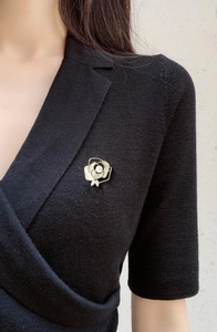 Close-up of a gold camellia brooch with white petals and a pearl on a black knit sweater