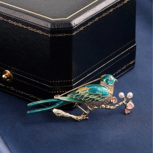 Vintage magpie brooch with green enamel, crystals, and pearls on a gold branch