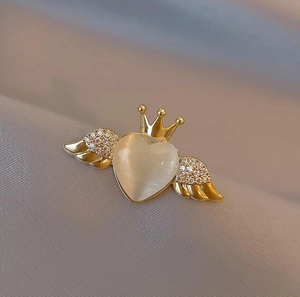 Elegant gold angel wing brooch with cream opal heart and crown on velvet background