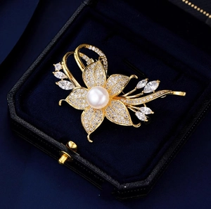 Elegante goldene Blumenbrosche mit weißer Perle und Kristallblüten auf blauem Samt